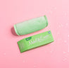 Rolled up Neon Green MakeUp Eraser next to packaging surrounded by water drops.