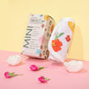 Rolled up Mini Wildflowers MakeUp Eraser cloth next to packaging, surrounded by flowers.