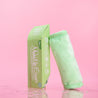 Rolled up Neon Green MakeUp Eraser cloth next to packaging surrounded by waterdrops.