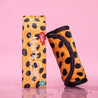 Rolled up Cheetah Print MakeUp Eraser next to packaging surrounded by waterdrops.