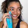 Woman smiling and holding a Fresh Turquoise MakeUp Eraser up to her face.
