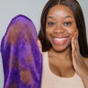 Woman smiling and holding up Queen Purple MakeUp Eraser after removing half her makeup.