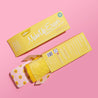 Front of Mellow Yellow MakeUp Eraser packaging next to the back of Mellow Yellow MakeUp Eraser packaging. The back of the packaging is open with a rolled-up Mellow Yellow MakeUp Eraser peeking out.