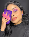 Woman holding Queen Purple 7-Day Set MakeUp Eraser cloth up to her face.